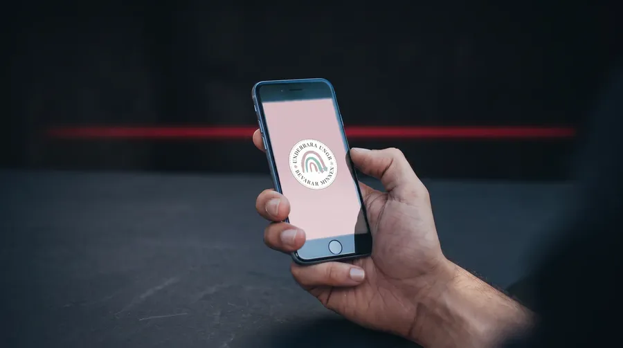 Mobiltelefon på ett träbord som visar Underbara Unges logotyp på rosa bakgrund